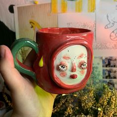 a hand holding a red coffee mug that has been decorated with eyes and noseballs