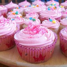 cupcakes with pink frosting and sprinkles on a wooden tray