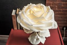 a large white rose sitting on top of a red book next to a brick wall