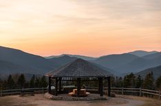 a gazebo in the middle of a field with mountains in the background at sunset