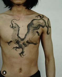 a man with a dragon tattoo on his chest is standing in front of a white wall