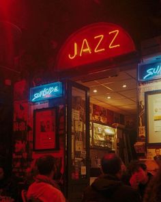 people sitting at tables in front of a restaurant with neon signs on the doors and windows