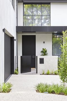 an entrance to a modern house with black doors and plants in the foregrounds