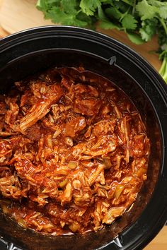 shredded meat in a slow cooker with parsley on the side and carrots next to it