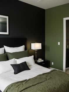 a bedroom with green walls and white bedding, black headboard and night stand