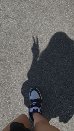 the shadow of a person's legs and shoes on asphalt with one hand up in the air