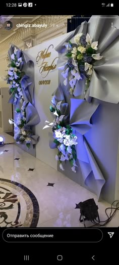 two large blue bows are on display in a building with white flowers and greenery