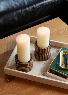 two candles are sitting in a tray on a table next to a book and some other items