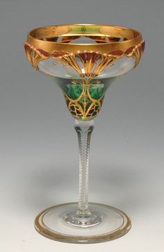 a wine glass with gold trimming and green designs on the rim, sitting on a white surface