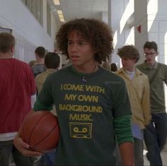 a young man holding a basketball while standing in a hallway with other people behind him