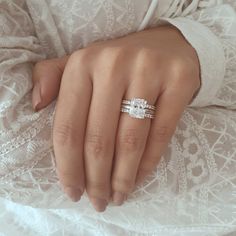 a woman's hand with two wedding bands on her fingers and an engagement ring in the other hand