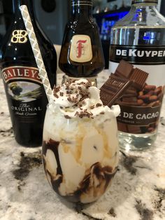 an ice cream sundae with chocolate and whipped cream in it next to bottles of booze