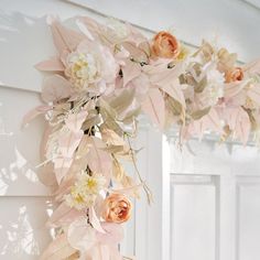 a wreath with flowers hanging from the side of a white door, in front of a mirror