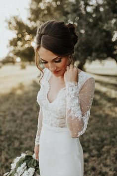 a woman in a white wedding dress holding a bouquet and looking down at her hand