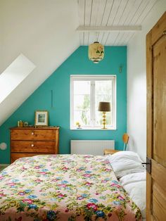 a bed sitting under a window in a bedroom next to a wooden dresser and lamp