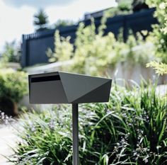 a mailbox sitting in the middle of some plants and bushes on a sunny day