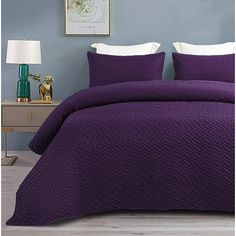 a bed with purple bedspread and pillows in a blue room next to a lamp