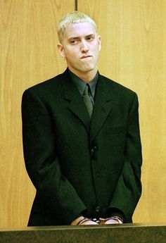 a man in a suit and tie standing next to a wooden paneled wall with his hands on his hips