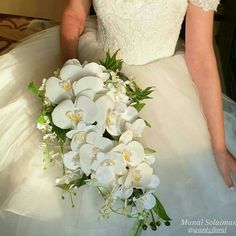 a woman in a wedding dress holding a bouquet of white orchids and greenery