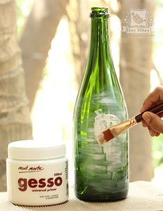 a person is painting a green bottle with white paint and a brush on the table