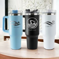 three travel mugs sitting on top of a wooden table next to each other,