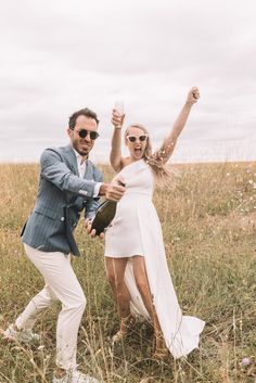 a man and woman are dancing in a field with one holding a wine glass while the other holds a bottle