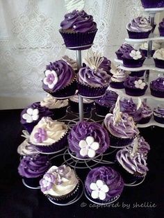 purple cupcakes with white flowers are arranged on a cake stand