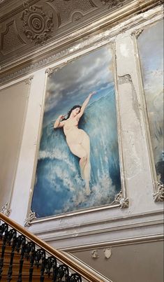 a large painting on the wall above a stair case in a building with ornate handrails