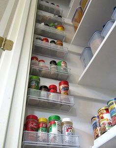 an open refrigerator door with canned food in the bottom shelf and labeled pantry storage below