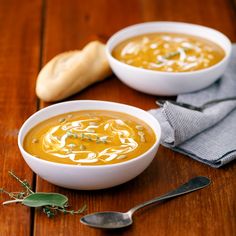 two bowls of soup are sitting on a wooden table next to a spoon and napkin