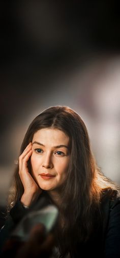 a woman with long hair is holding her hand to her ear and looking at the camera