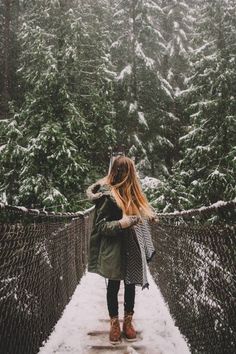 a woman standing on a suspension bridge in the middle of a forest with snow all around her