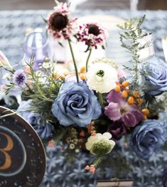 an arrangement of flowers on a table with plates and utensils in the background