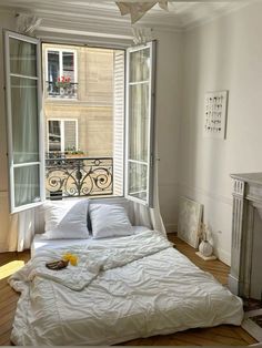 an unmade bed with white sheets and pillows in front of a window overlooking a balcony