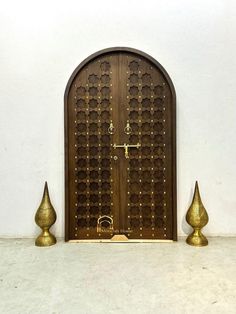 an ornate wooden door with two golden vases next to it on a white wall