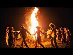 a group of people dancing around a fire with their hands in each others'arms