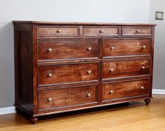 a wooden dresser sitting on top of a hard wood floor next to a white wall