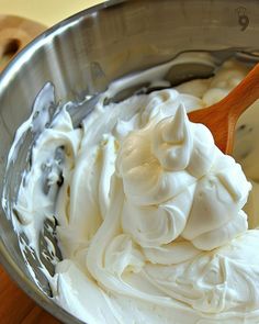 a bowl filled with whipped cream on top of a wooden table next to a spoon