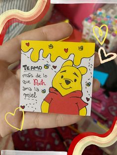 a hand holding a small card with winnie the pooh on it and hearts around it