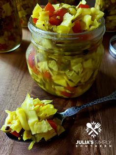 a glass jar filled with pickled vegetables on top of a wooden table next to two spoons