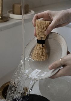 a person is holding a broom over a bowl in the bathroom while another hand holds it