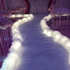 an aisle decorated with white feathers and pink flowers is lit up by fairy lights at the end