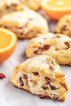 an orange and cranberry scones with icing next to some sliced oranges