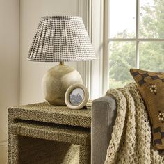 a lamp sitting on top of a wooden table next to a window with a blanket