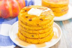 stack of pumpkin pancakes with butter on top sitting on a plate next to an apple