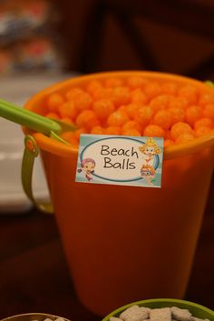 there is a bucket full of orange balls and two bowls filled with white rocks on the table