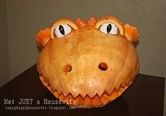 a close up of a pumpkin shaped like a dinosaur's face with big eyes