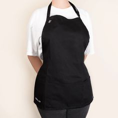 a woman wearing an apron standing in front of a white wall with her hands on her hips