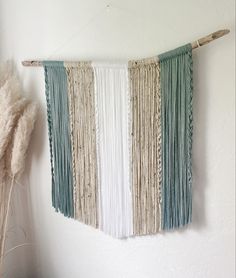 a wall hanging made from yarn and wood sticks with some dried flowers in the corner