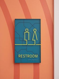 a restroom sign on the wall in front of an orange and blue striped wallpaper